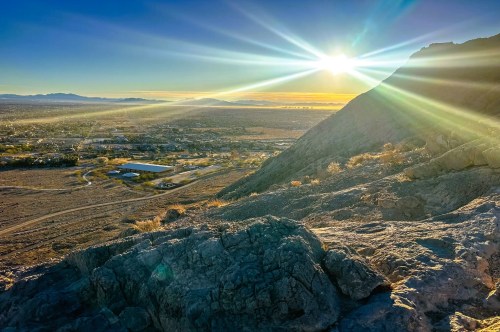 A rugged mountain landscape at sunset with views of a city below and rolling hills in the backdrop