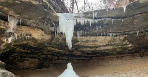 A frozen waterfall in a rocky cavern, with a large central icicle and an ice mound forming on the ground.