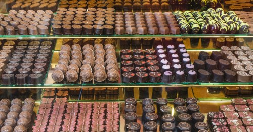 A glass display case is filled with perfectly arranged rows of gourmet chocolates and truffles featuring intricate designs and patterns at Katherine Anne Confections in Chicago.