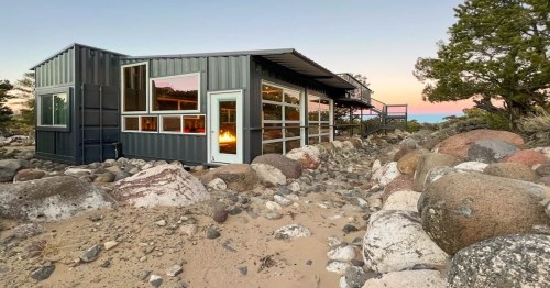 a grey luxury shipping container airbnb with several windows near a rocky path in utah