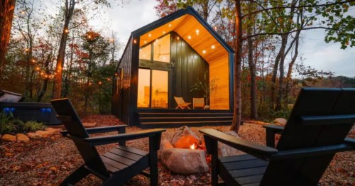 A gorgeous warm-hued cabin sits behind a firepit with two seats in the scenic Hocking Hills region of Ohio.