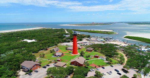 large orange-red lighthouse situated in the middle of grassy land and small homes in florida