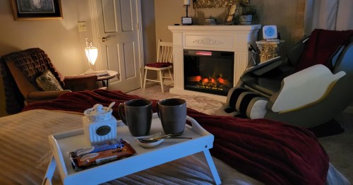 Cozy bedroom featuring a white fireplace, massage chair, and a breakfast tray with coffee mugs.