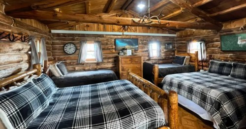 The bedroom of a gorgeous log cabin Airbnb rental in North Dakota with wooden walls, floors and ceiling. The beds have black and white flannel sheets.