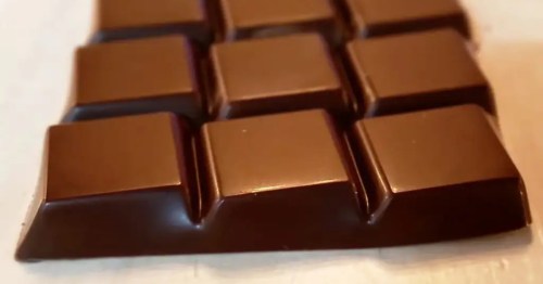 A close-up shot of a chocolate bar reveals its perfect squares, smooth texture, and rich, dark color. The focus is on the satisfying grid pattern, highlighting the treat's classic and tempting appearance.