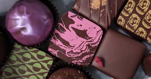 An overhead shot of vibrant, artisanal chocolates in various colors and patterns, nestled in a gift box.