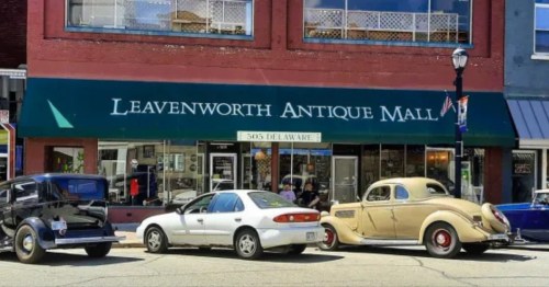 Historic downtown Leavenwoth Kansas showing the storefront of an antique mall with vintage cars parked outside.  