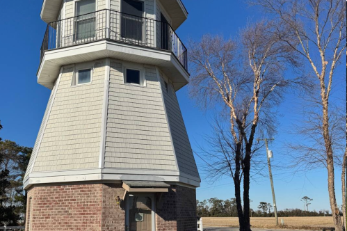 Exterior of a lighthouse in North Carolina, with a door at ground level and a wrap around balcony