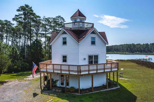 Exterior of a lighthouse Airbnb in Virginia, with blue skies and green grass