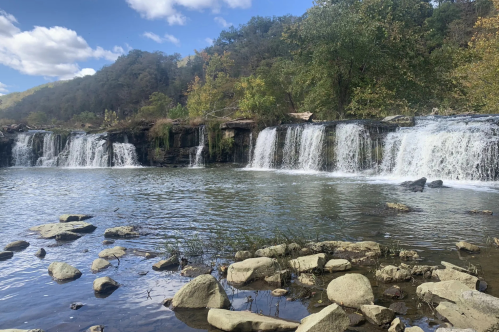 Waterfall in West Virginia, with crashing water surrounded by green trees and blue skies