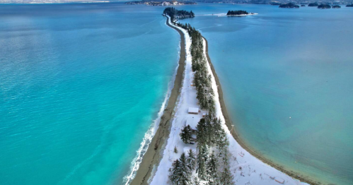 A narrow strip of land stretches between two bright turquoise bays in the Alaskan wilderness.