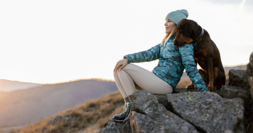 Woman and her dog, taking a break from hiking in the mountains and looking at the view and enjoying the winter sun.