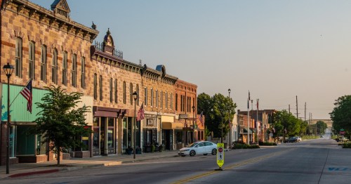 Historic brick buildings and American flags line a quiet, sunny Main Street in downtown Chadron, Nebraska.
