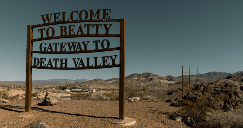 a sign stating "welcome to beatty gateway to death valley" stands in the desert of nevada