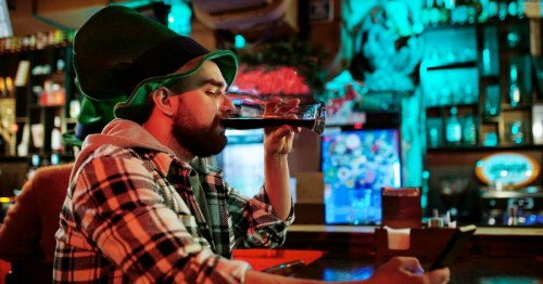 A man sitting at the bar in an Irish pub in Georgia, drinking a dark colored beer from a glass.