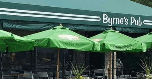 Byrne's Pub exterior with green awnings and umbrellas, tables visible through windows and a black metal fence.
