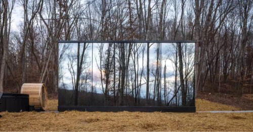 Rectangular mirror-sided Hocking Hills Airbnb reflecting a forest of bare trees, next to a sauna and hot tub.