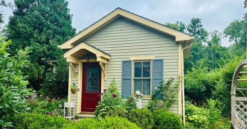 Charming green cottage vacation rental in Frenchtown, NJ, with a red door, blue shutters, and lush garden setting.