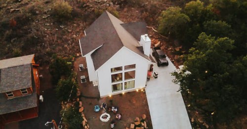 aerial shot of a modern white house and guests surrounding the fire pit in the yard in medicine park, oklahoma