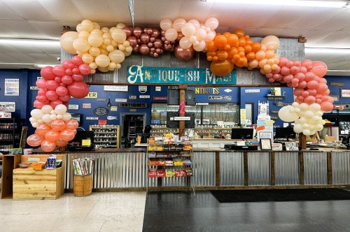 The front counter of an antique mall in Missouri with a blue wall and large sign decorated with a colorful balloon arch