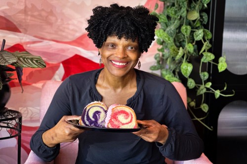 The owner of Sister Honey's, a woman-owned bakery in Orlando, smiling while holding a plate with decadent cake slices