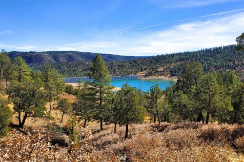 A gorgeous view from a hiking trail inside Lincoln National Forest in NM featuring a pretty turquoise lake and a mix of forestry and mountains in the distance