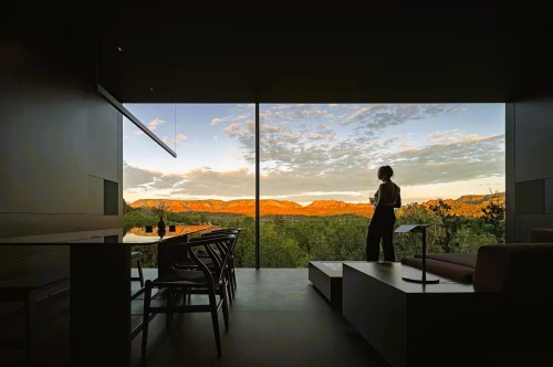 Telescope House Airbnb in Arizona with a woman standing in front of a massive glass wall with gorgeous views of the desert landscapes in the distance
