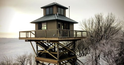 Warmly lit A-frame SD cabin glows at night. A picnic table sits on the grass, surrounded by silhouetted trees.