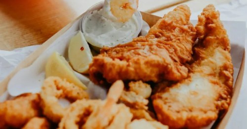 Fried fish and shrimp in a box, hand dipping a shrimp into sauce.