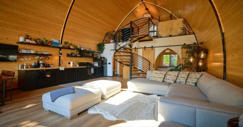 a large two-story loft cabin with white couches, a spiral staircase, and cozy decor