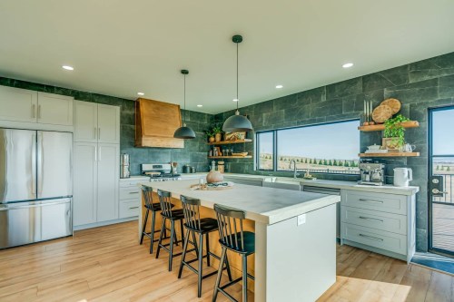 a large white kitchen island with four bar stools, a teal backsplash, and window