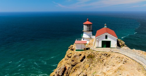 Point Reyes Lighthouse on a rocky cliff overlooking the blue Pacific Ocean in Northern California.