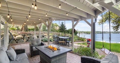 a covered porch with seating, a fire pit table, and a swing with lake views in illinois