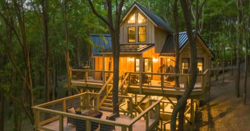 Illuminated treehouse with wooden decks, located in Deep Creek Lake, Maryland, surrounded by a dense forest.