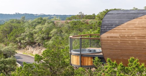 side exterior view of the spyglass treehouse with a hot tub on the balcony and trees surrounding the rental
