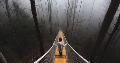 A woman walks down a suspension bridge to a cliffside cabin in Kentucky.