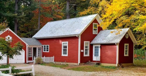 The exterior of "The Little Red Schoolhouse" Airbnb property in Granby, Connecticut. The red building is surrounded by trees with colorful autumn leaves.