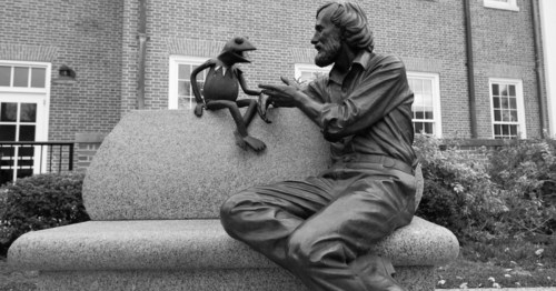 A black and white shot of The Jim Henson Memorial at the University of Maryland College Park campus. The bronze statue depicts Henson sitting on a bench engrossed in conversation with Muppet, Kermit the Frog.