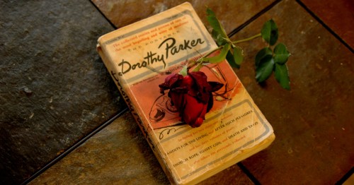A vintage book titled "The Portable Dorothy Parker" sits on a stone surface with a single red rose.