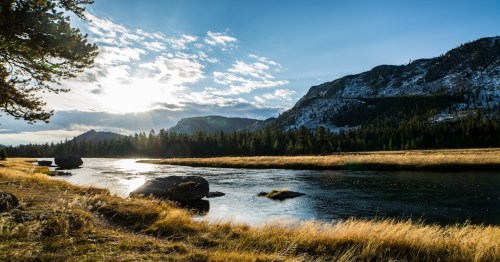 a view of the Yellowstone River with grassy land, cloudy skies, and mountains in the back