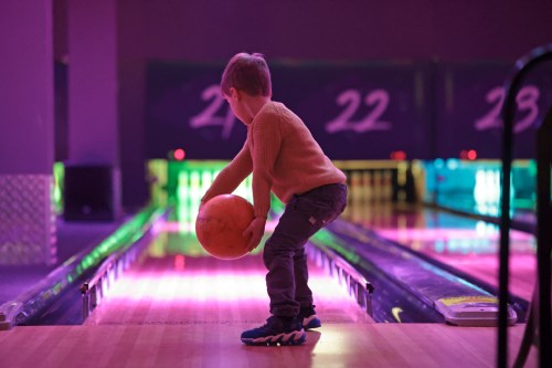Young boy bowls ball in bowling alley, pink light on bowling alley