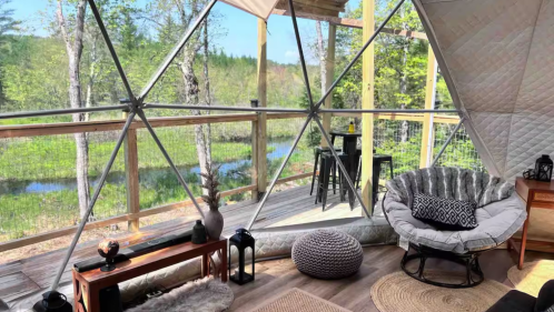 The living room at the StreamSide Getaway Geo Dome Airbnb in Buckfield, Maine. The domed room looks out upon a porch, stream, and wooded area.