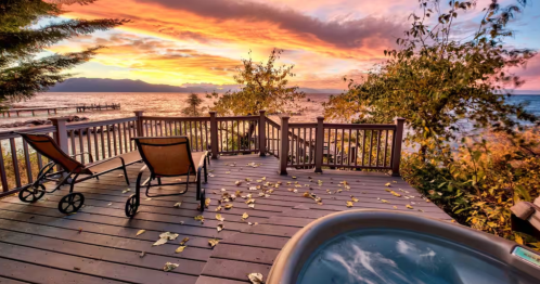 a hot tub and lounge chairs on a wooden deck overlooking a beautiful yellow, orange, and pink sunset