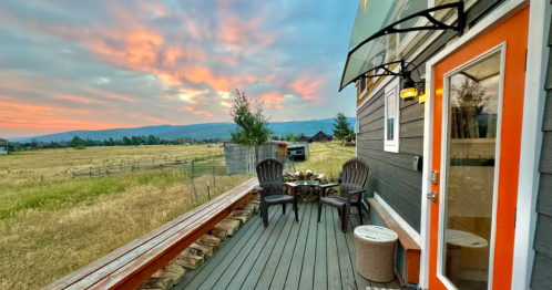 the exterior of a tiny home in idaho with chairs on the front deck and a pink and blue sky covering the background