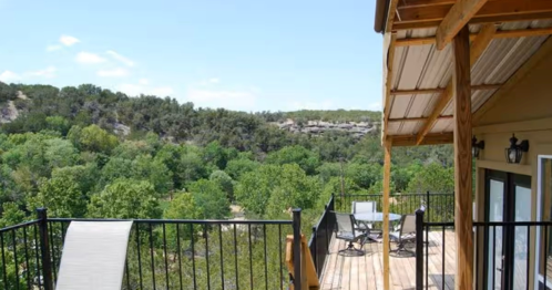 exterior photo of a cabin in oklahoma with an outdoor upper deck and a green forest in the background