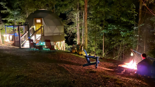 Nighttime view of a dome Airbnb in Kentucky surrounded by woods and a fire pit area