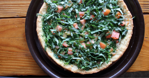 A delicious-looking pizza with cornmeal crust is garnished with fresh basil and generous slices of heirloom tomato.