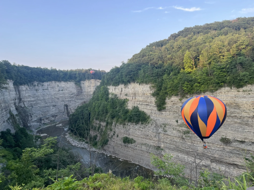 View of Letchworth State Park gorge with a colorful hot air balloon against the steep rock walls. River visible below.