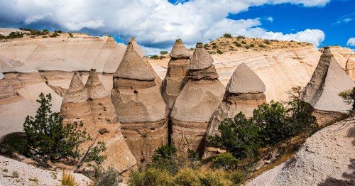 cone-shaped rock formations near forest trees under a cloudy sky