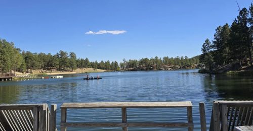A view of a lake from a dock with a small beach and kayakers on the water.